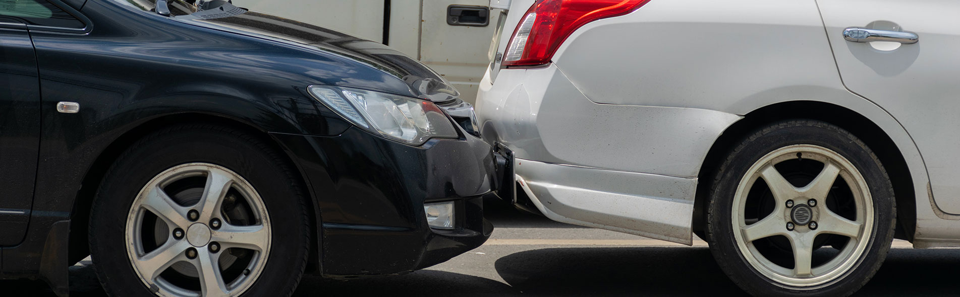 A silver car having been hit by a black car in a rear-end collision