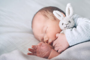 A newly born baby asleep while holding a stuffed bunny