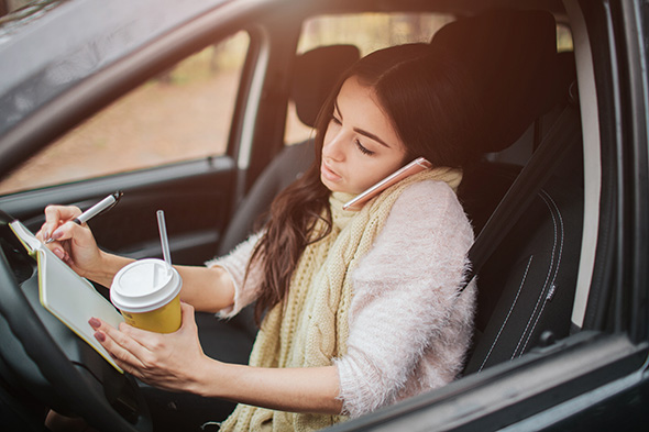  A woman drives while on the phone and taking notes on a notepad, clearly distracted