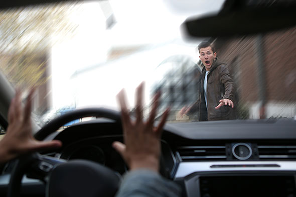 A man in a brown jacket looks surprised as the car is about to cause a pedestrian accident