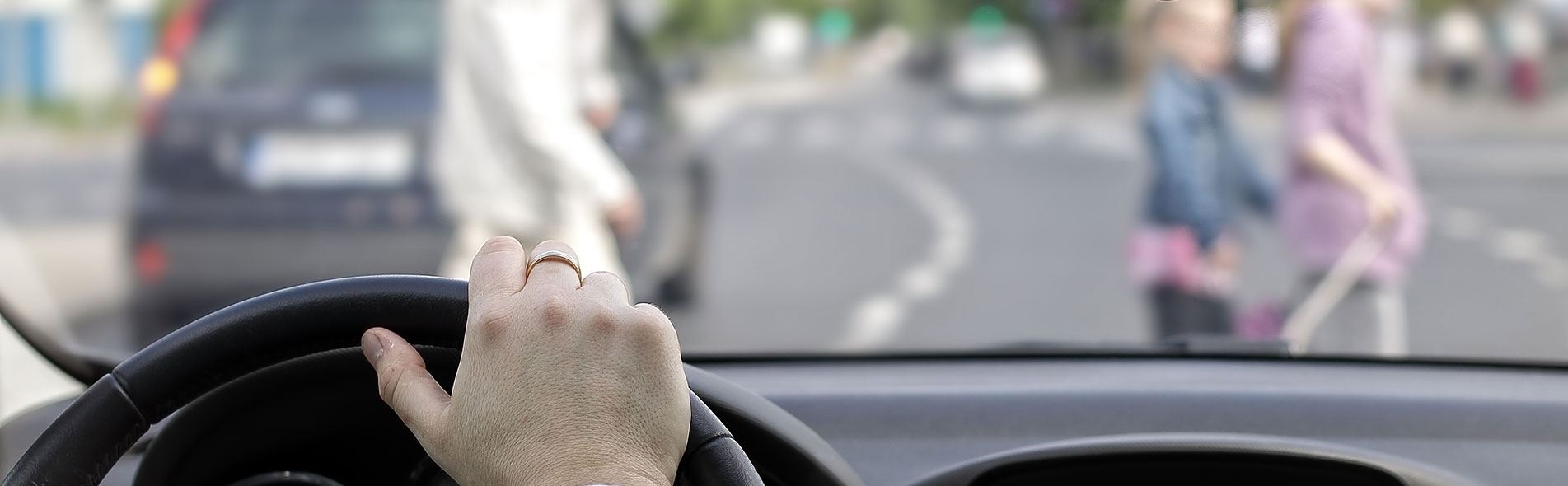 A man in a car stopped at a crosswalk with an older man and two girls crossing the street