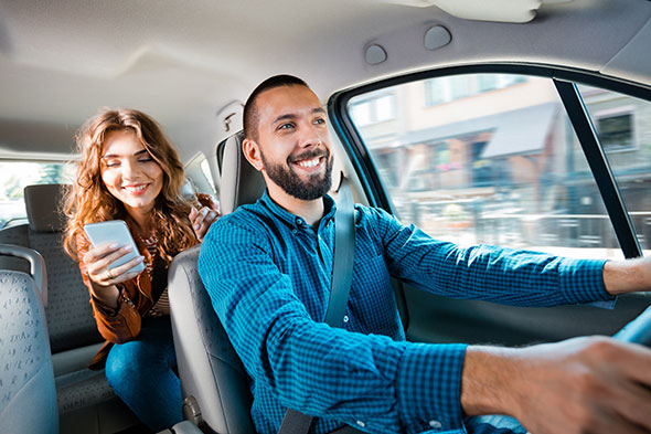 Smiling male uber driver with female passenger on her phone in the back seat