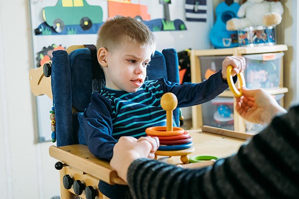 Activities for kids with disabilities. Preschool Activities for Children with Special Needs. Boy with with Cerebral Palsy in special chair play with mom at home.