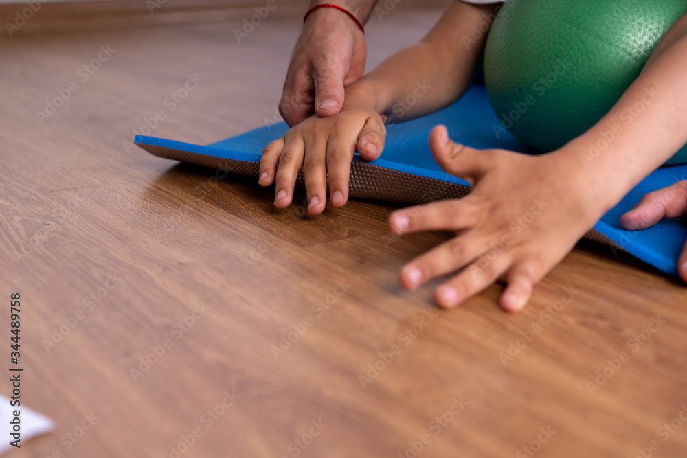 A kid with Cerebral Palsy stretches out their arms over a foam ball and mat